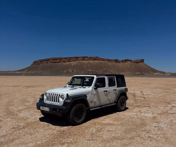 eep Wrangler blanc sur un lac asséché avec plateau rocheux en arrière-plan dans le sud marocain