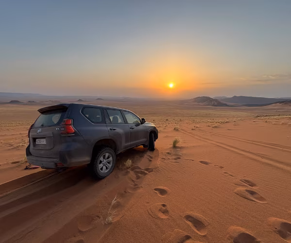 Toyota Land Cruiser Prado TX gris sur une dune au coucher du soleil dans le désert du Maroc