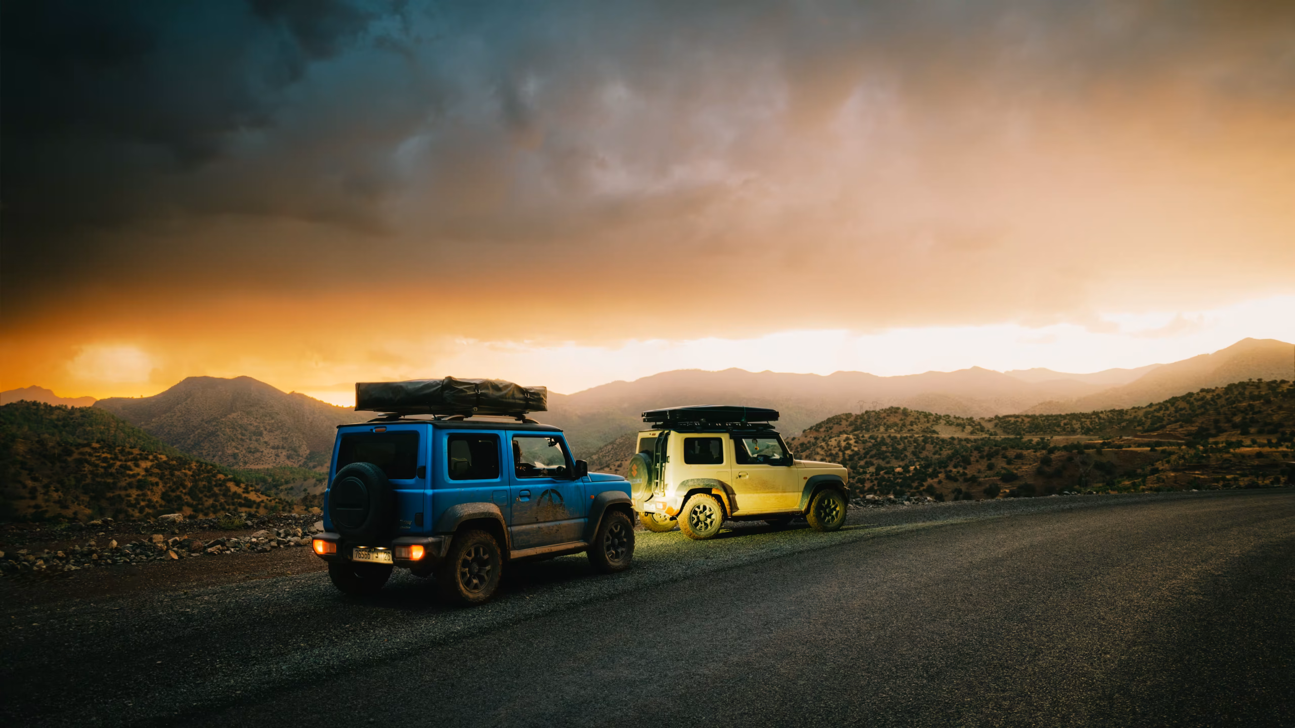 Deux Suzuki Jimny, équipés de tentes de toit, garés sur le bas-côté d'une route de montagne